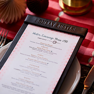 bombay bustle menu typed on paper boarded with molly mahon tuk tuk pink design pictured in its setting on the restaurant table on top of a molly mahon luna pink linen table runner