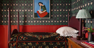 Bedroom with black and green tulip floral wallpaper, bed with patterned bedding, and a lamp.