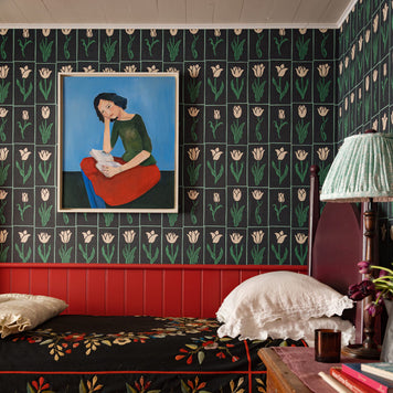 Bedroom with black and green tulip floral wallpaper, bed with patterned bedding, and a lamp.