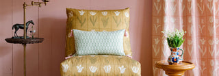 Decorative chair with patterned cushions against a pink wall with floral designs.