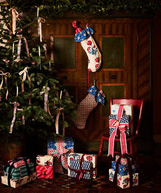 Image of a Christmas tree, with presents wrapped in Molly Mahon fabric placed underneath and on a chair to the side, two filled Molly Mahon stockings hanging on the wall in the back.