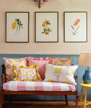 Decorative living room with floral pillows on a bench, framed botanical prints on the wall, and a lamp.