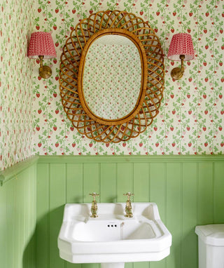 Vintage-style bathroom with wicker mirror, floral wallpaper, and green paneling.