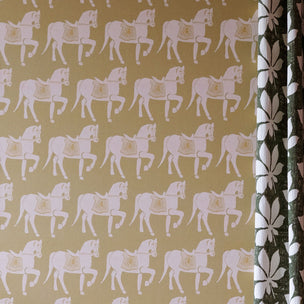 A close-up of wallpaper featuring a repeating pattern of horses on a warm mustard-yellow background, with a second patterned fabric or wallpaper swatch visible along the right edge.