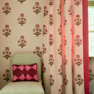 A styled interior corner showing patterned curtains and matching wallpaper. The curtains are light pink with a repeating brown floral motif and a solid coral-pink border.