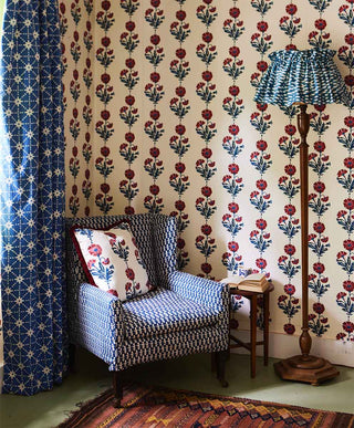 Image of a room with molly mahons dianthus wallpaper in midnight iron on the wall. To the left a window with a curtain in molly mahons stars fabric in indigo and next to the window a armchair upholstered in molly mahons bagru fabric in indigo and on the armchair a cushion covered in molly mahons dianthus fabric in iron indigo colours. 