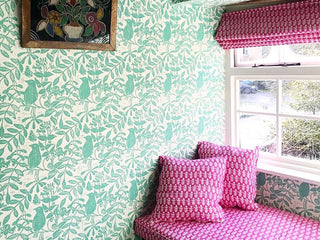 a bedroom window seat in a bedroom decorated in molly mahon's birds and bees pea green wallpaper and the seat cushions upholstered in bagru pink with a matching curtain blind